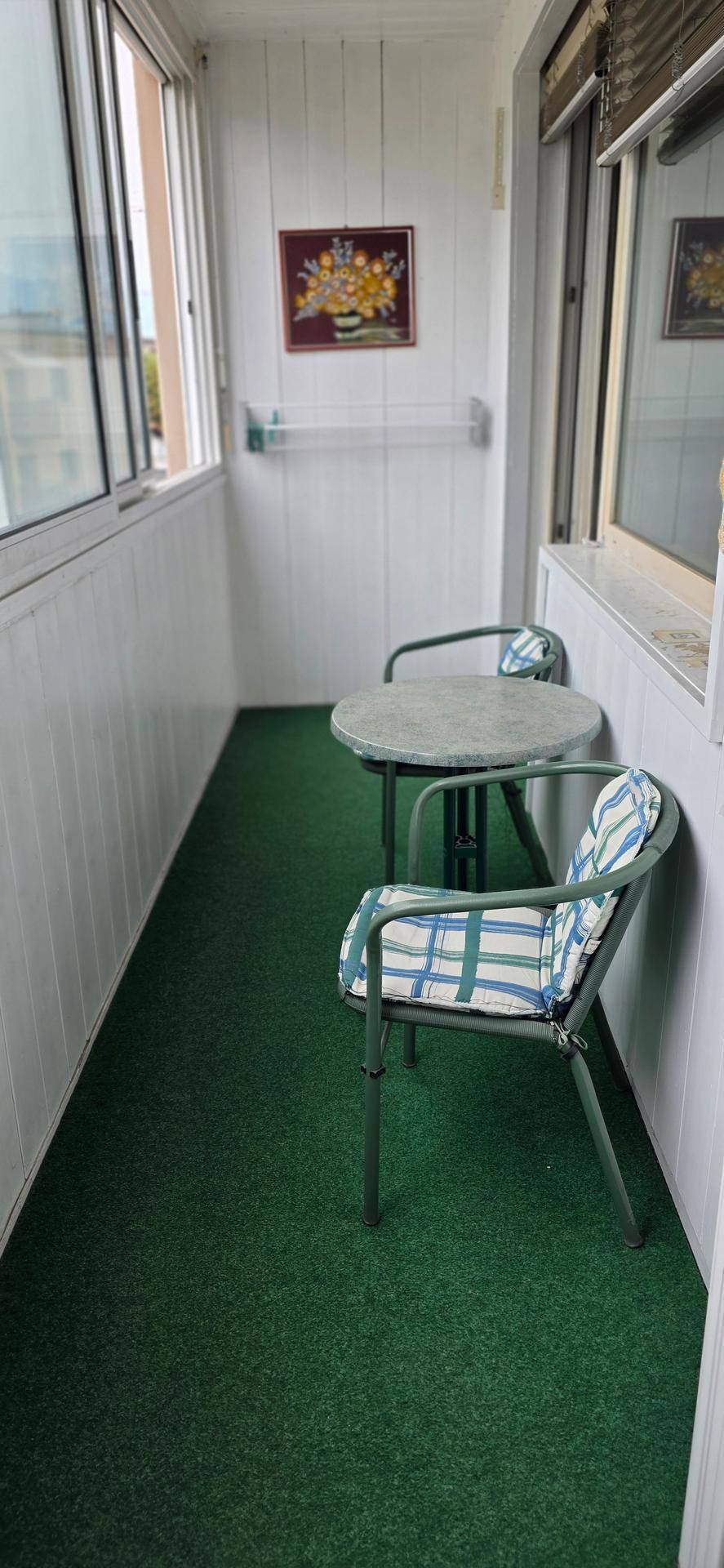 Verglaster Balkon mit grünem Teppichboden und kleiner Sitzgruppe, ideal für entspannte Stunden.