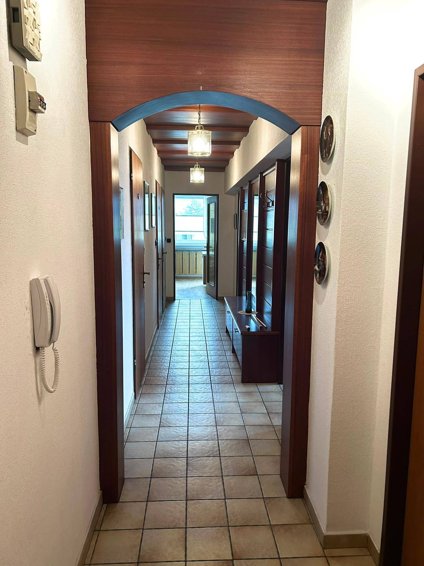 Heller Flur mit Fliesenboden und Holzelementen, der zu einem Balkon oder einer Loggia führt.