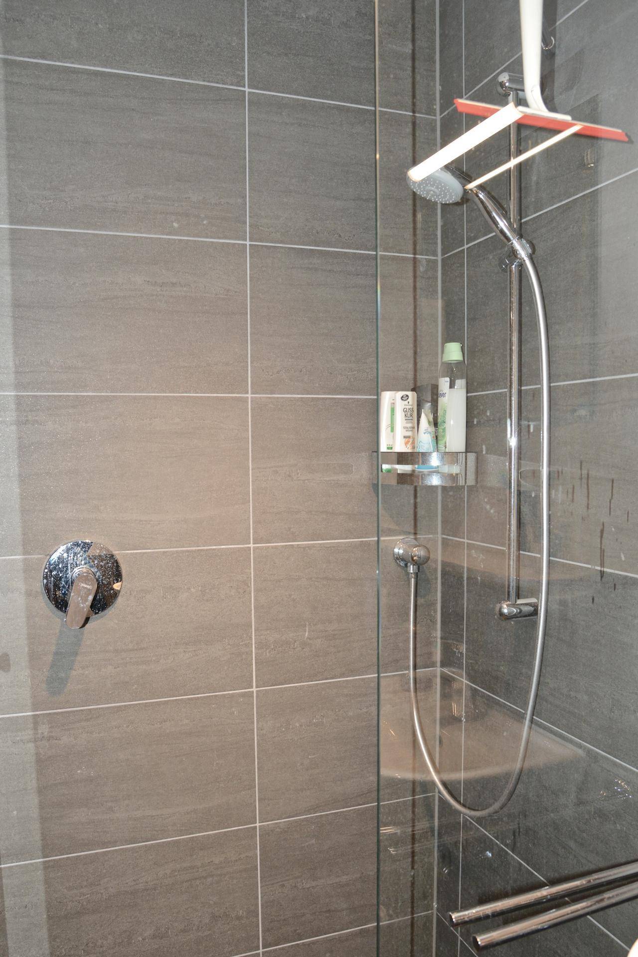 Moderne Duschkabine mit grauen Fliesen und Handbrause in einem gepflegten Badezimmer.