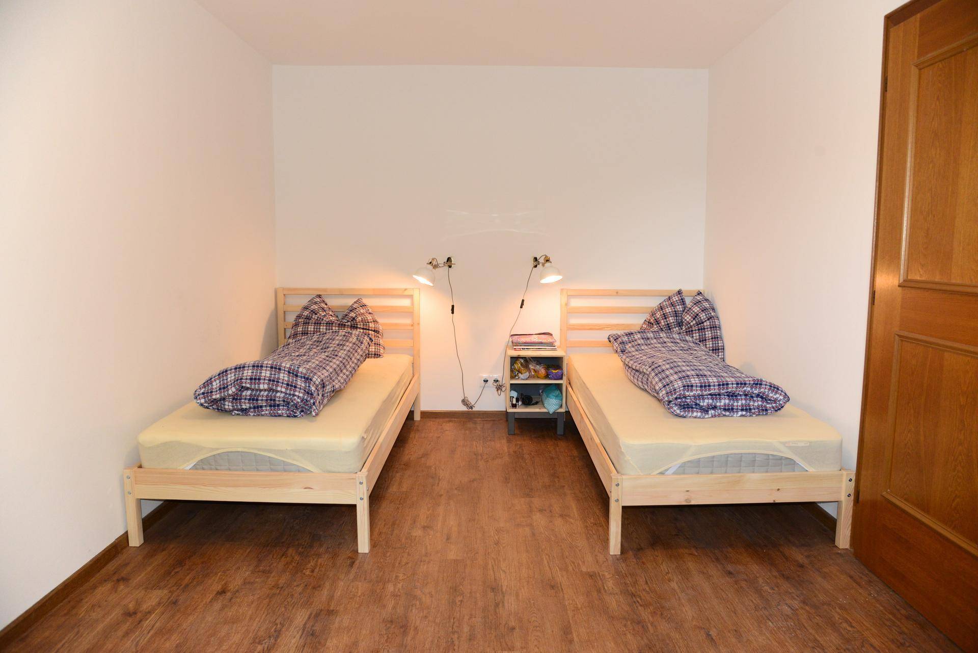 Helles Schlafzimmer mit zwei Einzelbetten, Holzboden und einfacher Einrichtung.