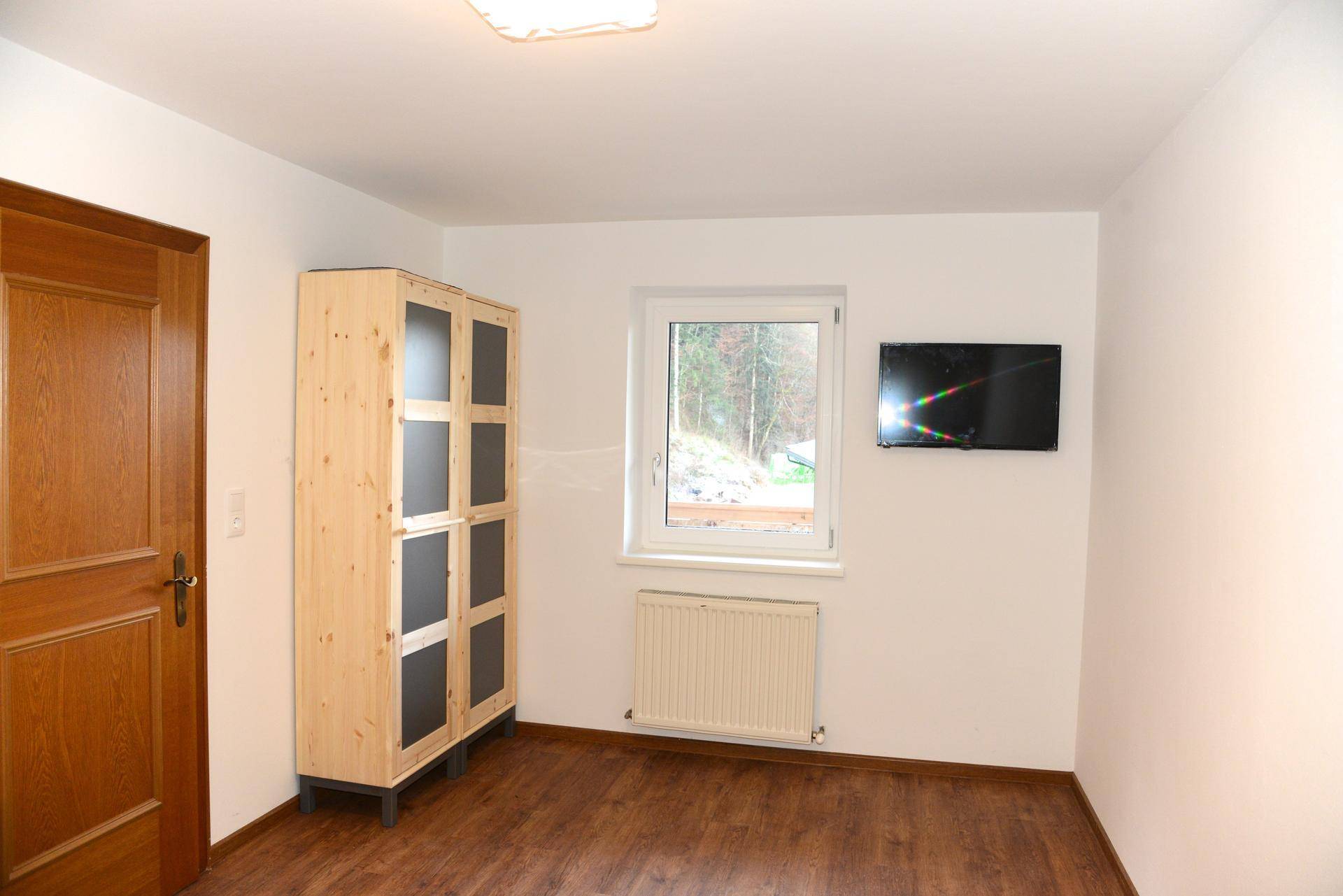Heller Raum mit Fenster, Heizkörper und einem Holzschrank, ideal als Schlaf- oder Gästezimmer.