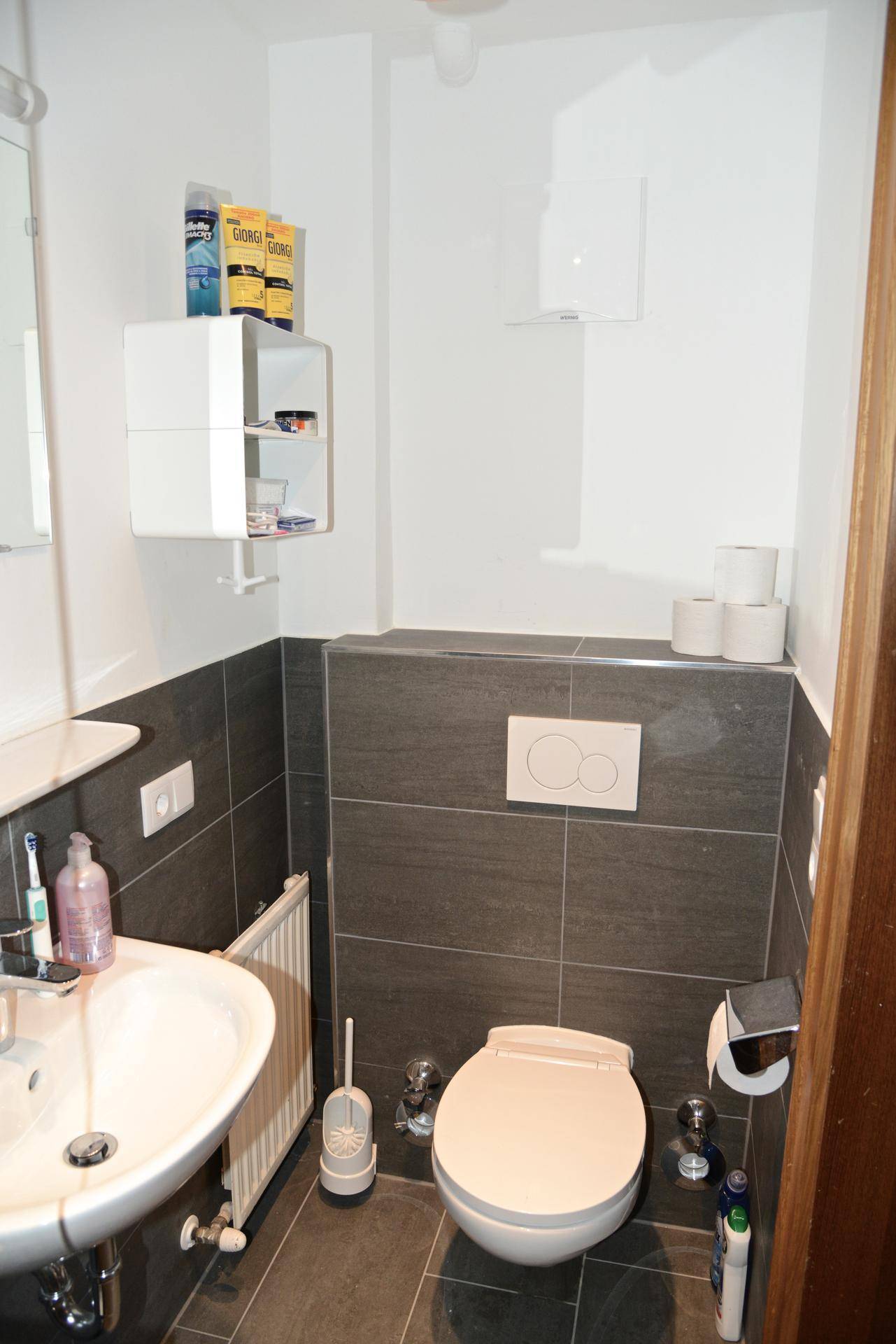 Kleines Badezimmer mit WC, Waschbecken und modernen grauen Wandfliesen.