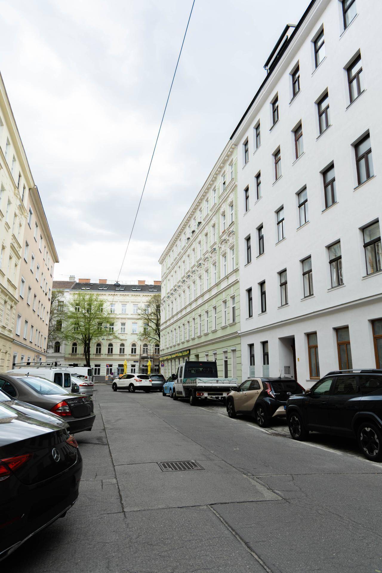 Eine belebte Stadtstraße mit parkenden Autos und hohen Wohngebäuden unter einem bewölkten Himmel.