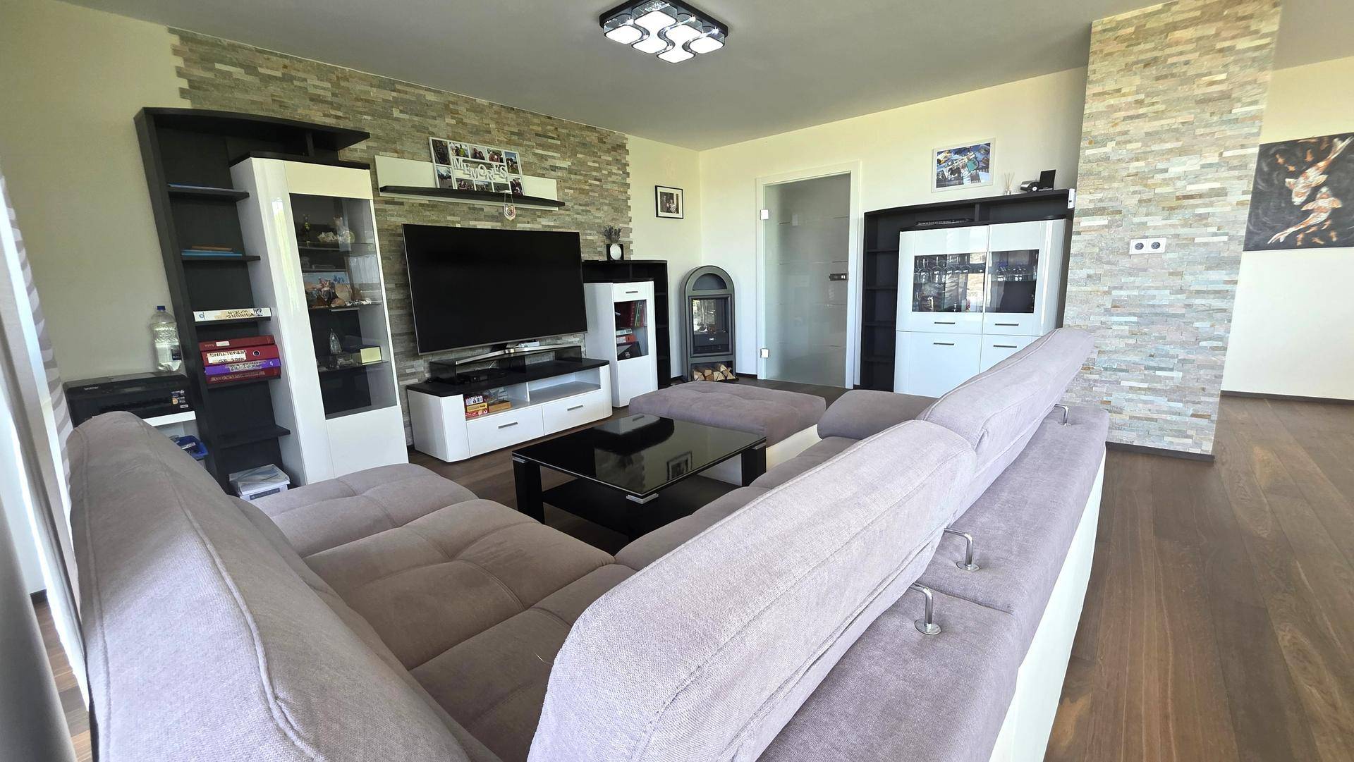 Gemütliches Wohnzimmer mit großem Sofa, TV-Möbeln und einem modernen Kaminofen.