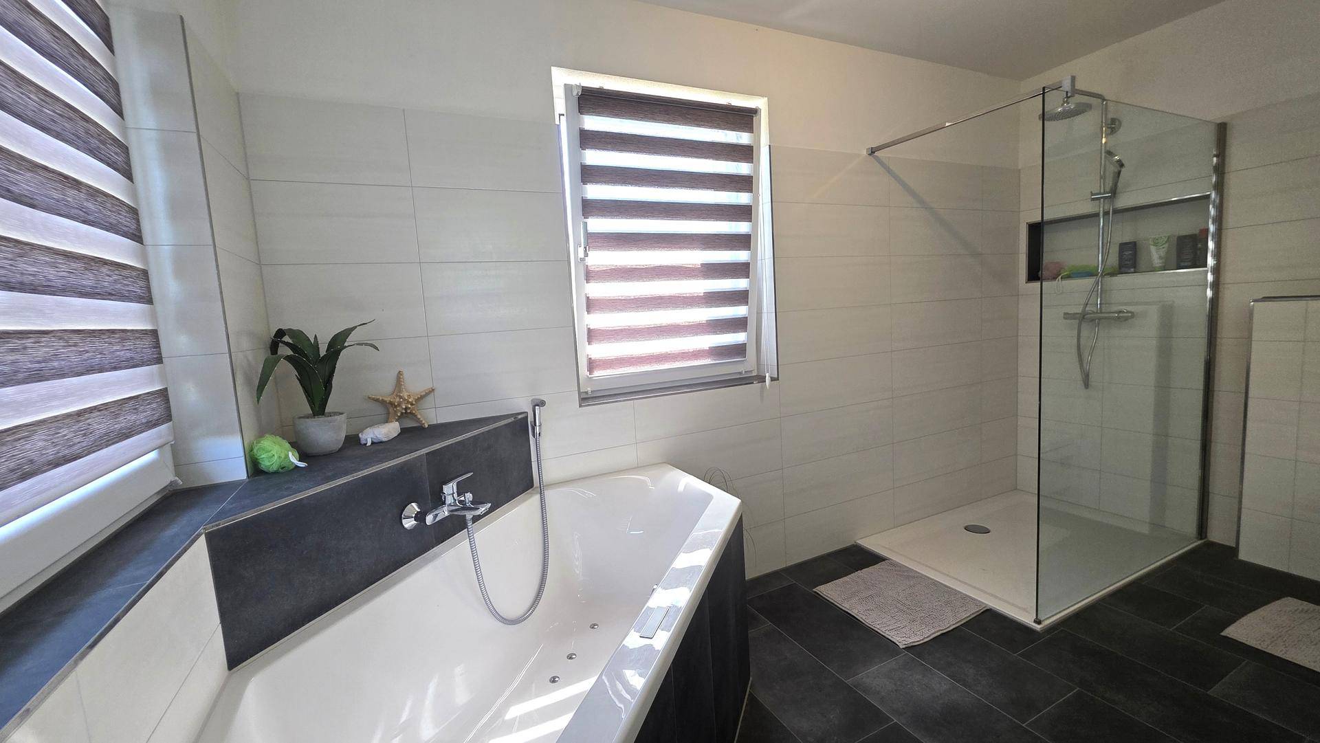 Geräumiges Badezimmer mit Eckbadewanne, ebenerdiger Dusche und Fenster.
