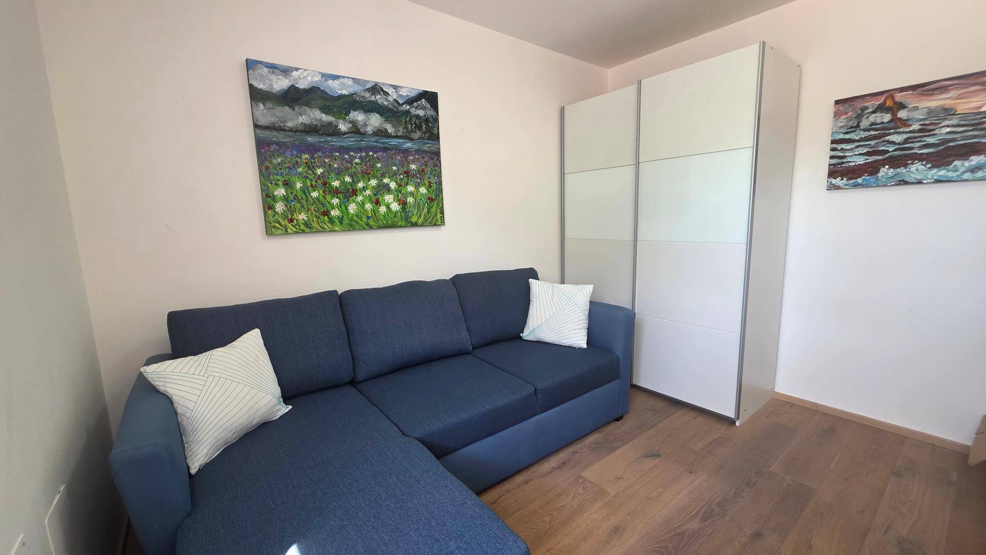 Helles Arbeitszimmer mit blauem Ecksofa und weißem Kleiderschrank.