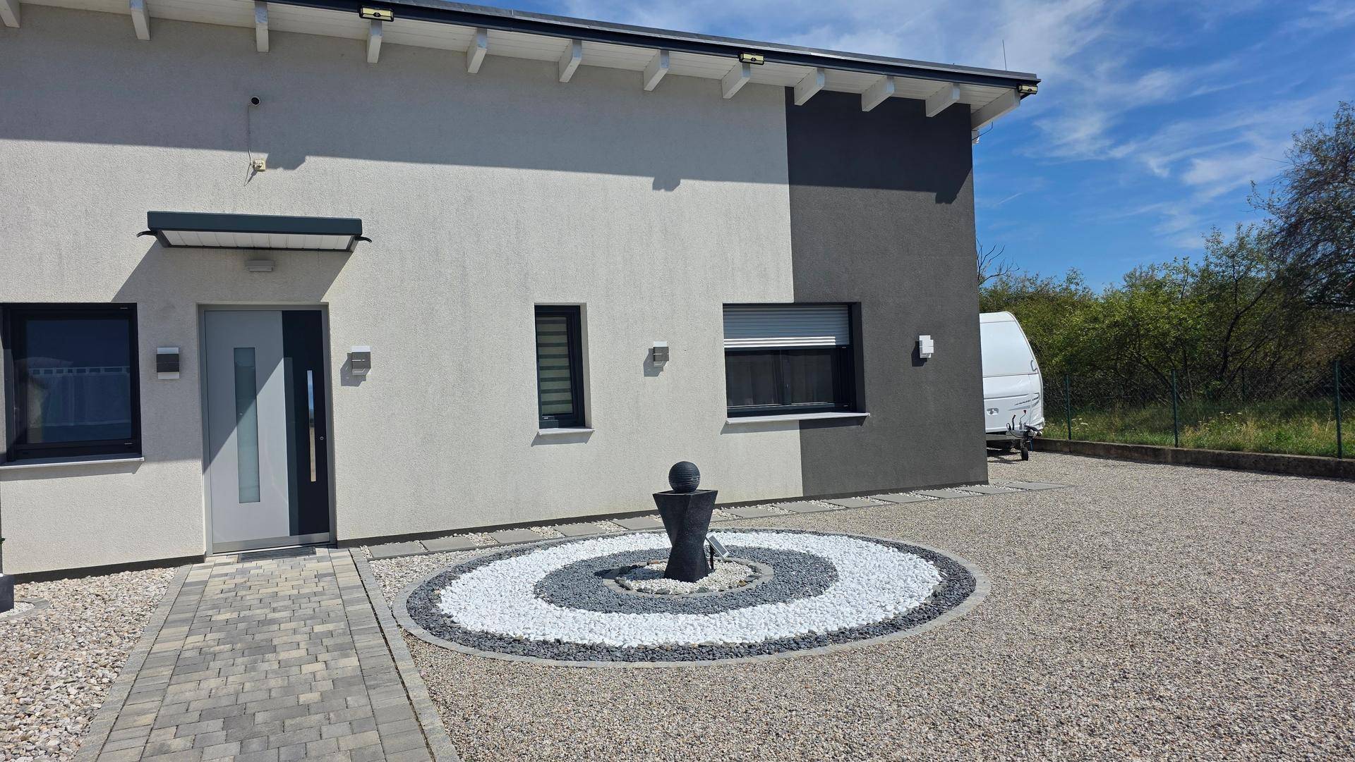 Eingangsbereich des Hauses mit moderner Haustür und dekorativem Kiesgarten mit Brunnen.
