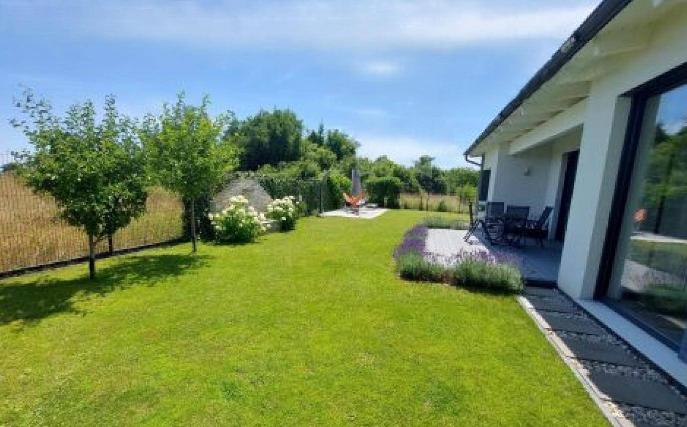 Weitläufiger Garten mit Rasenfläche, jungen Bäumen und einer kleinen Terrasse mit Lavendelbepflanzung am Haus.