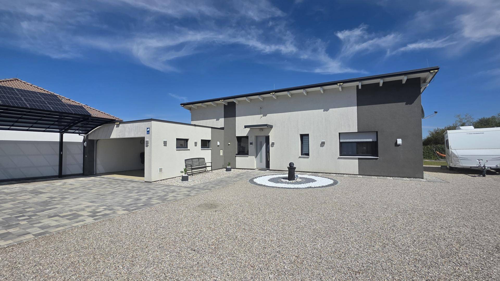 Ansicht des modernen Einfamilienhauses mit Carport, gepflegtem Vorgarten und Kiesfläche.