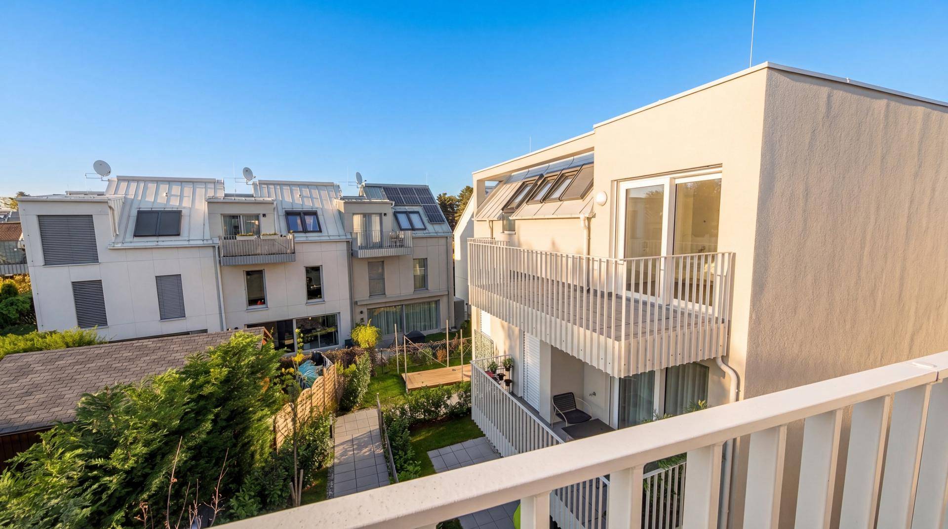 Moderne Wohngebäude mit Balkonen und Dachfenstern in sonniger Umgebung.