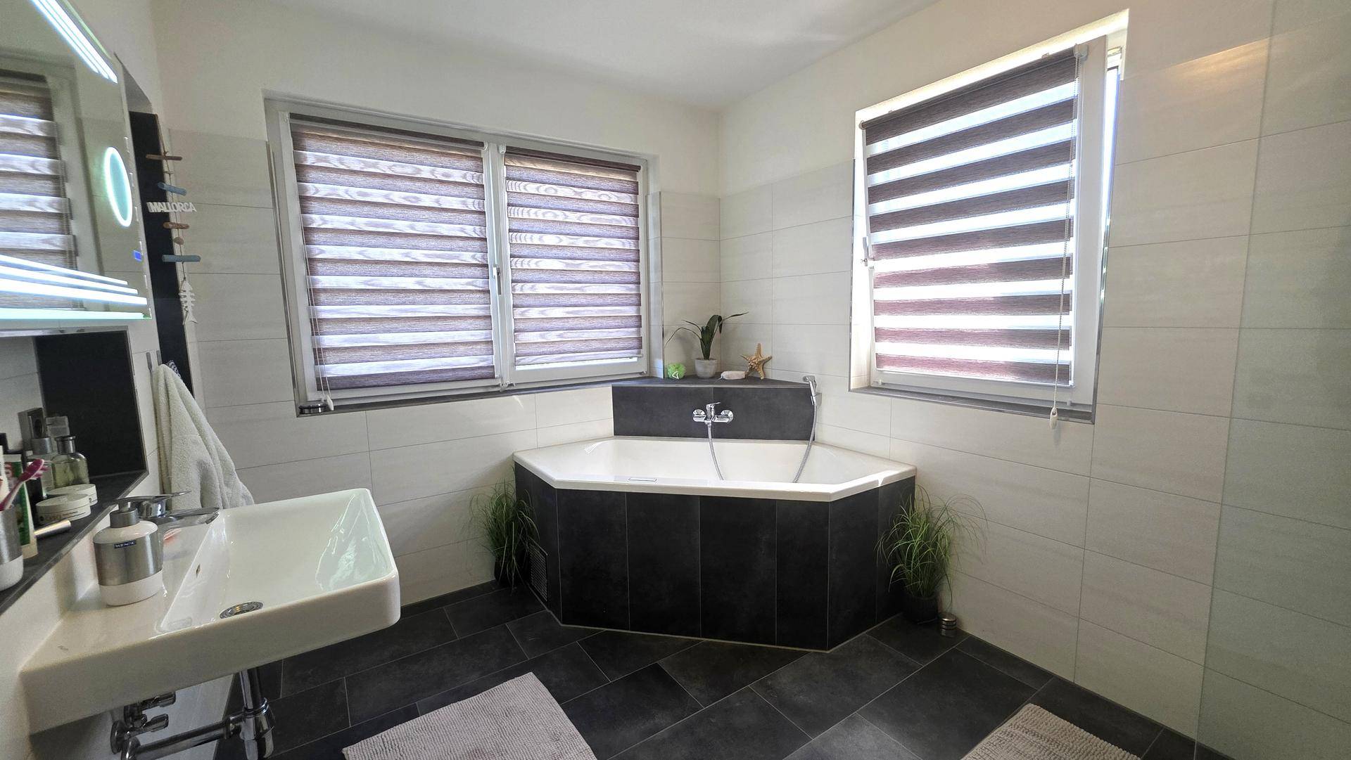Modernes Badezimmer mit Eckbadewanne, Einzelwaschbecken und zwei Fenstern.