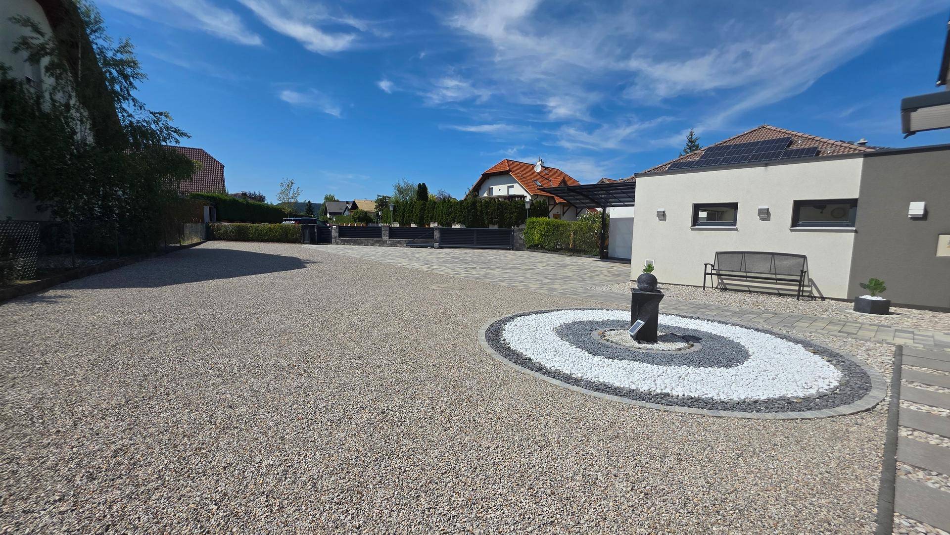 Weitläufige Kiesauffahrt vor dem modernen Einfamilienhaus unter strahlend blauem Himmel.