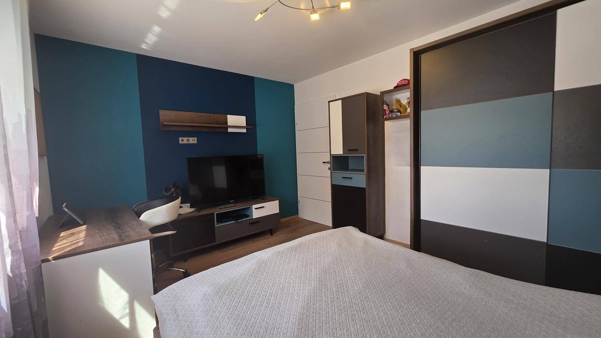 Schlafzimmer mit großem Kleiderschrank, TV-Bereich und farbiger Wandgestaltung.