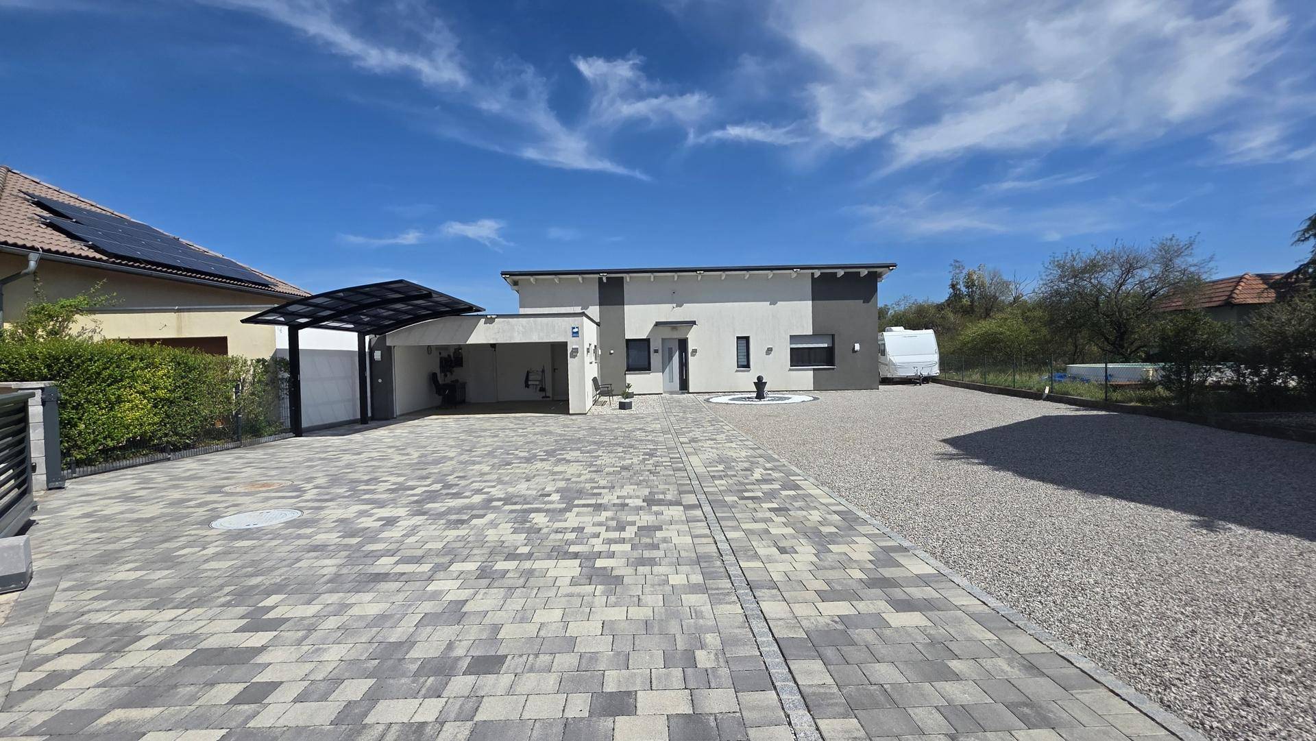 Modernes Einfamilienhaus mit Carport und gepflasterter Zufahrt unter blauem Himmel.