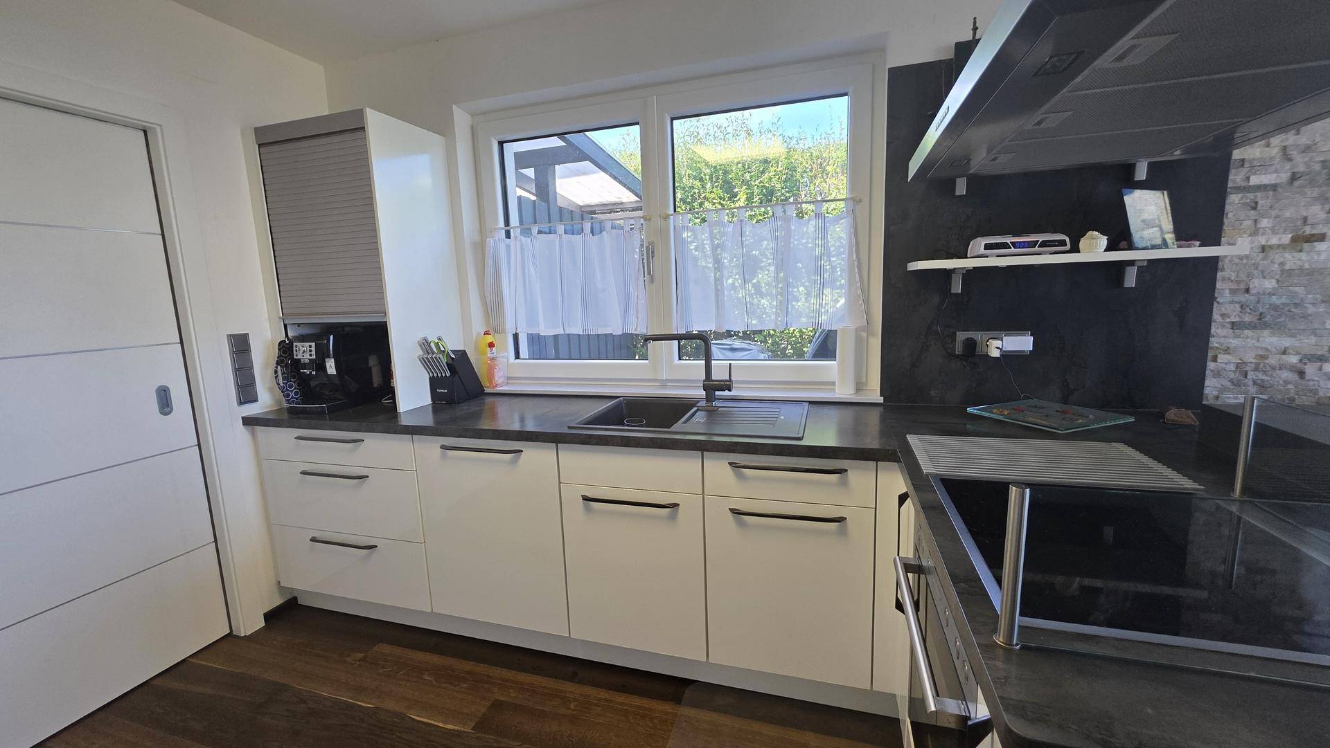 Funktionale Küche mit Spülbereich unter dem Fenster und modernen weißen Schränken.