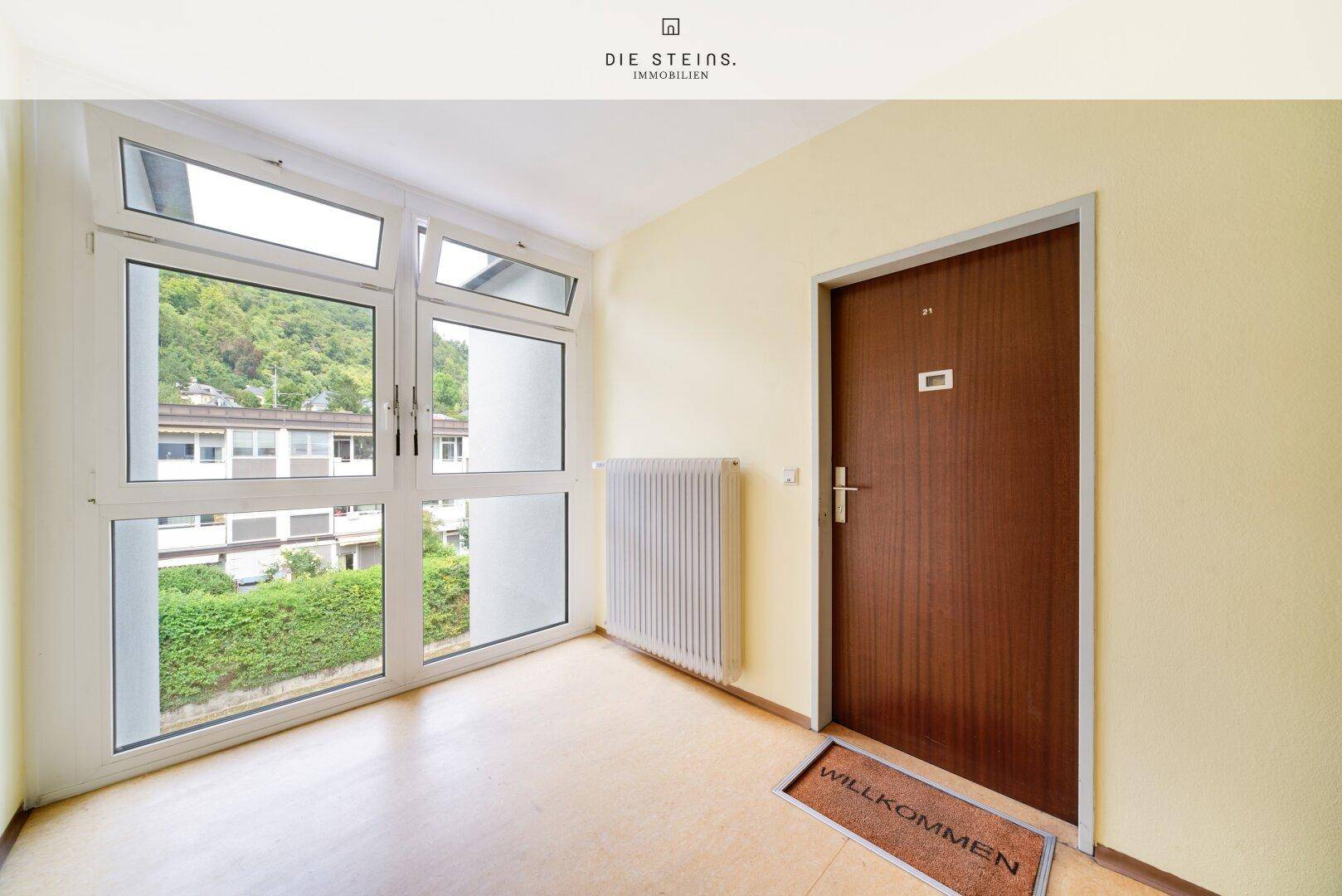 Heller Eingangsbereich mit großer Fensterfront und einer robusten Holztür, die zum Apartment führt.