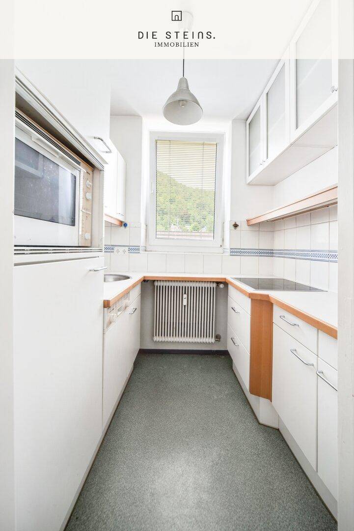 Funktionale Küche mit weißen Schränken, Holz-Arbeitsplatten und einem Fenster mit Blick ins Grüne.