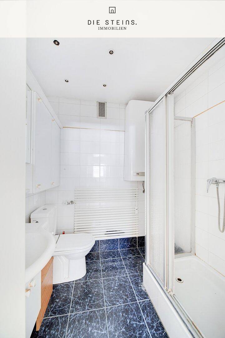 Badezimmer mit Dusche, WC und Waschbecken, ausgestattet mit dunklen Fliesen und weißen Wänden.