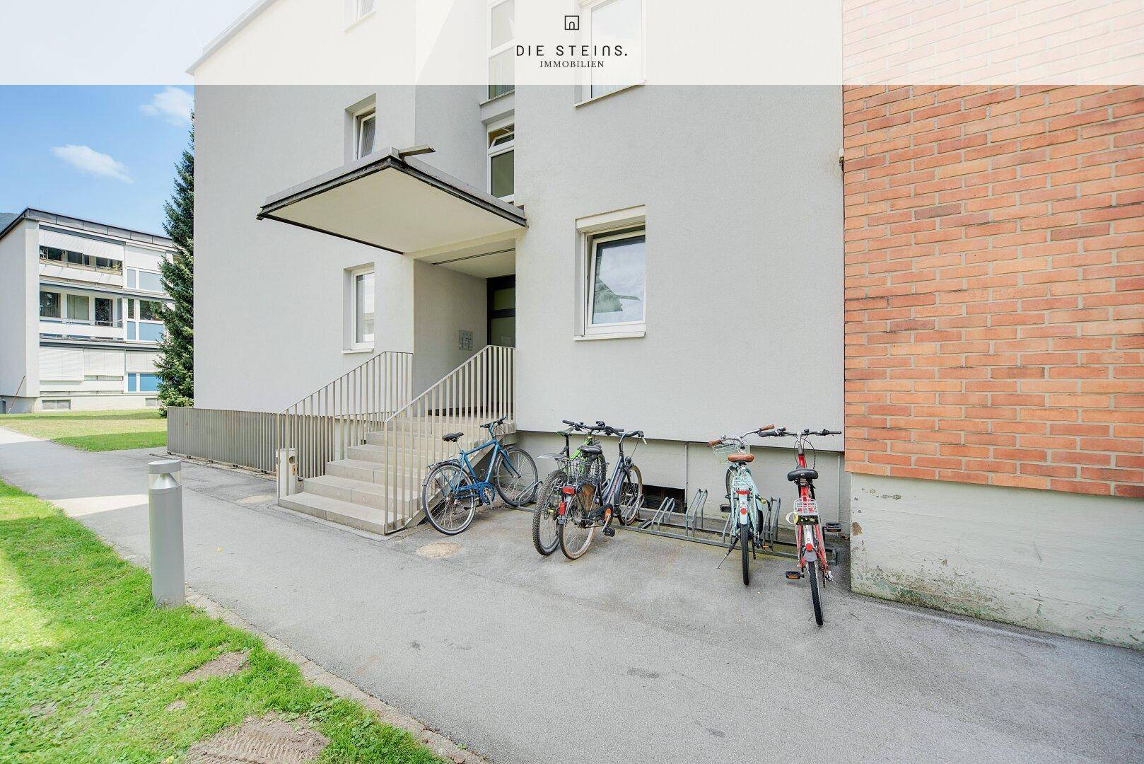 Eingangsbereich eines Mehrfamilienhauses mit Fahrradständern und Treppenzugang.