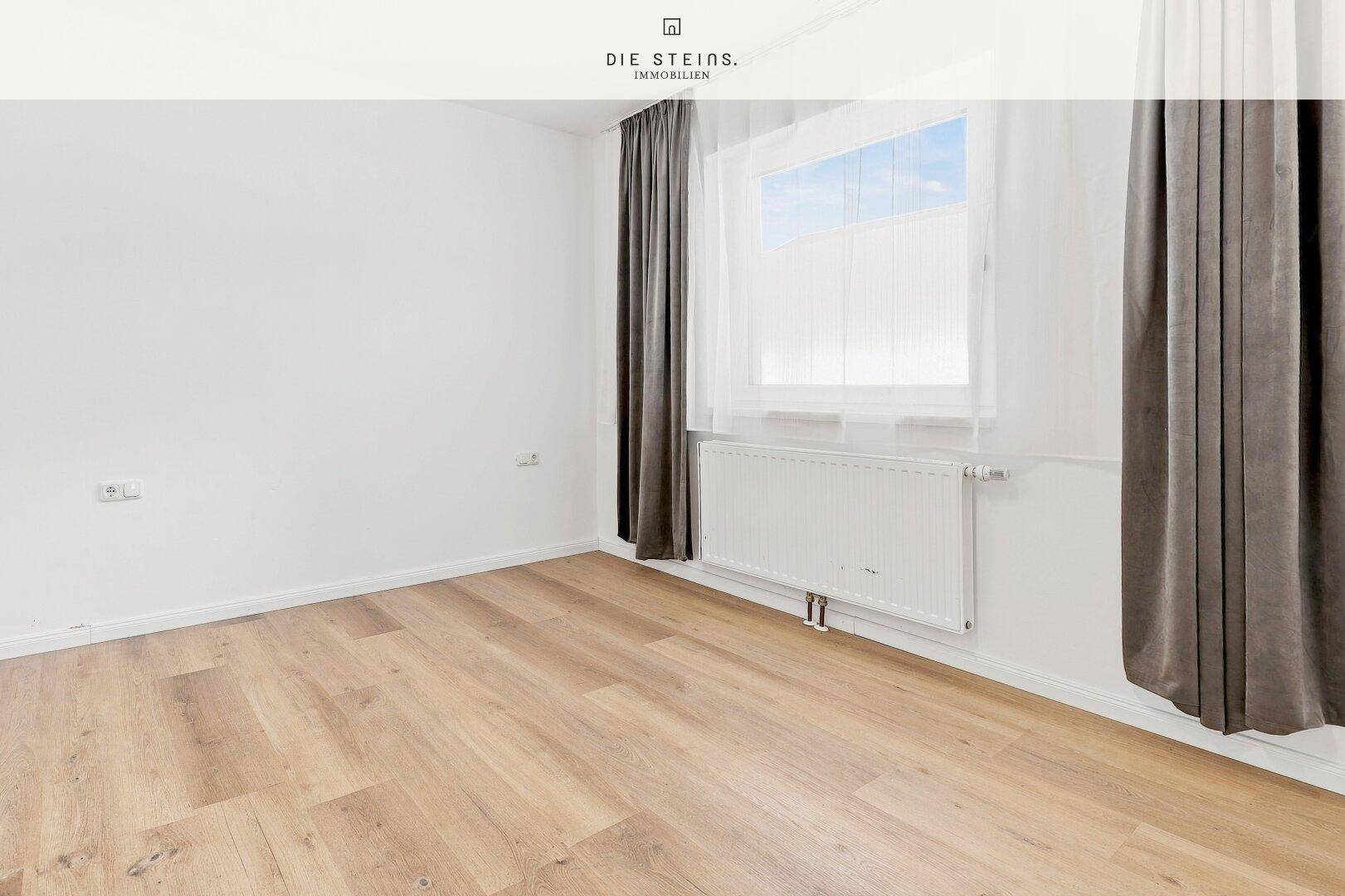 Schlafzimmer mit hellem Laminatboden, weißen Wänden und einem Fenster mit dunklen Vorhängen.