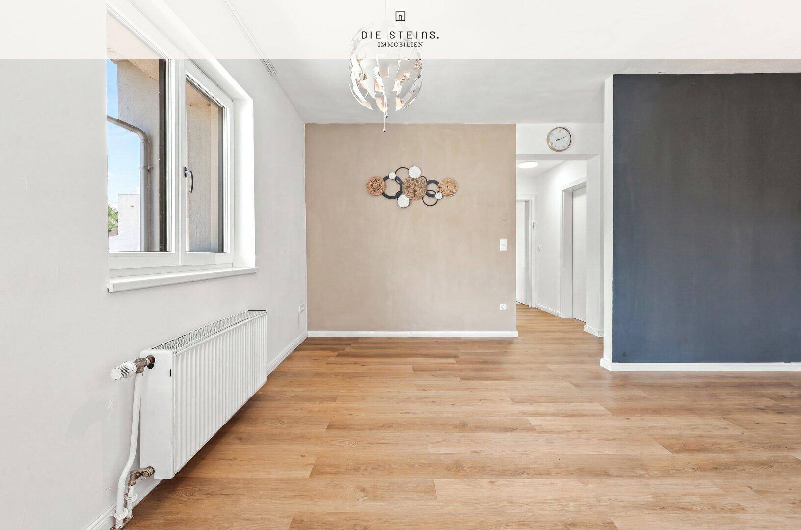 Geräumiger Wohnbereich mit Laminatboden, hellen Wänden und einem dekorativen Akzent an der Wand.