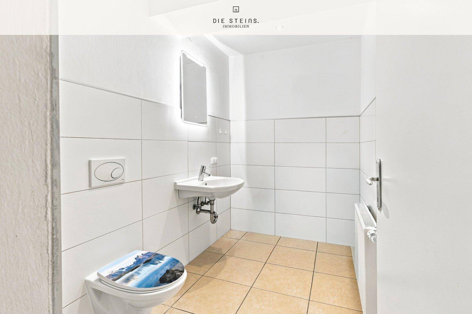 Helles Gäste-WC mit weißen Fliesen, modernem Waschbecken und beleuchtetem Spiegel.
