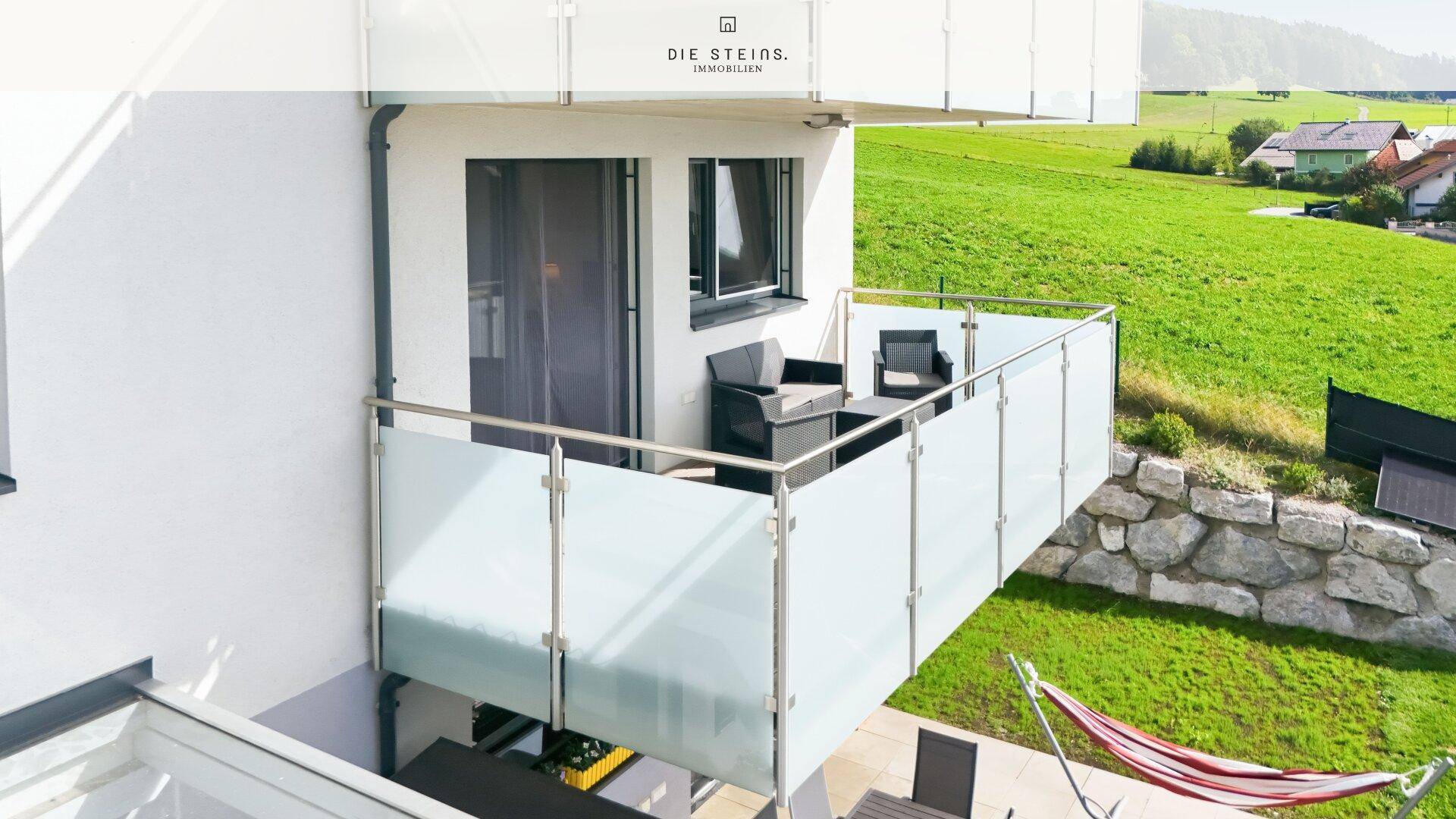 Möblierter Balkon mit Glasbrüstung und weitem Blick ins Grüne.