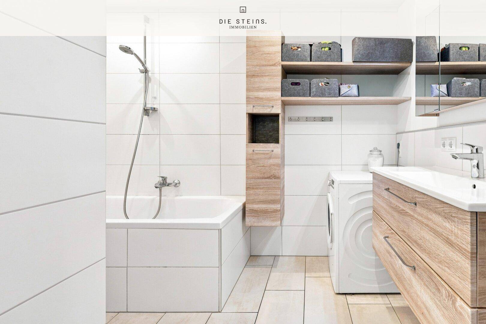 Helles Badezimmer mit Badewanne, Waschmaschine und Holzwaschtisch.