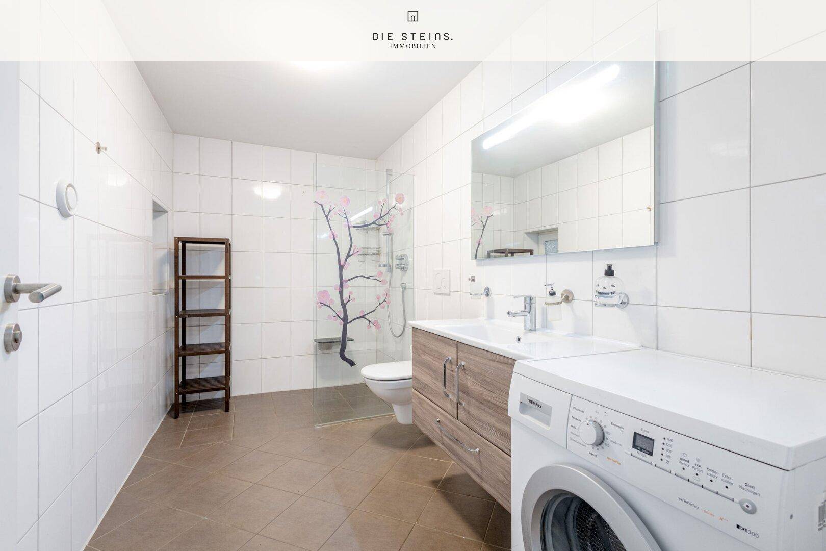 Modernes Badezimmer mit weißen Fliesen, Dusche und Waschmaschine.