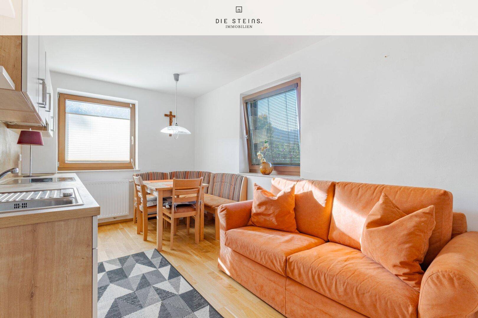 Gemütlicher Wohn-Essbereich mit kleiner Küchenzeile, orangefarbenem Sofa und Holzboden.