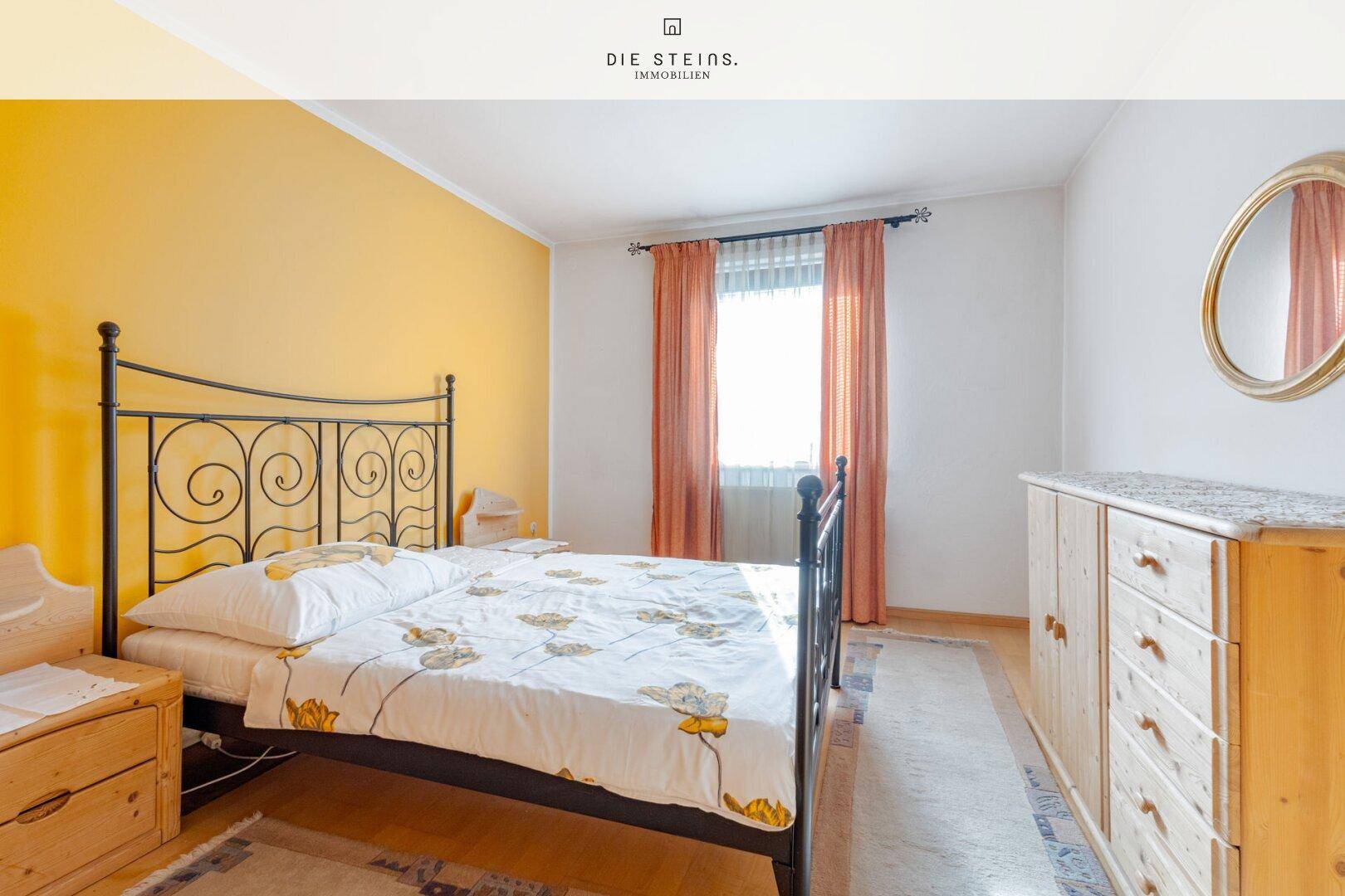 Schlafzimmer mit gelber Akzentwand, schmiedeeisernem Bett und Holzboden.