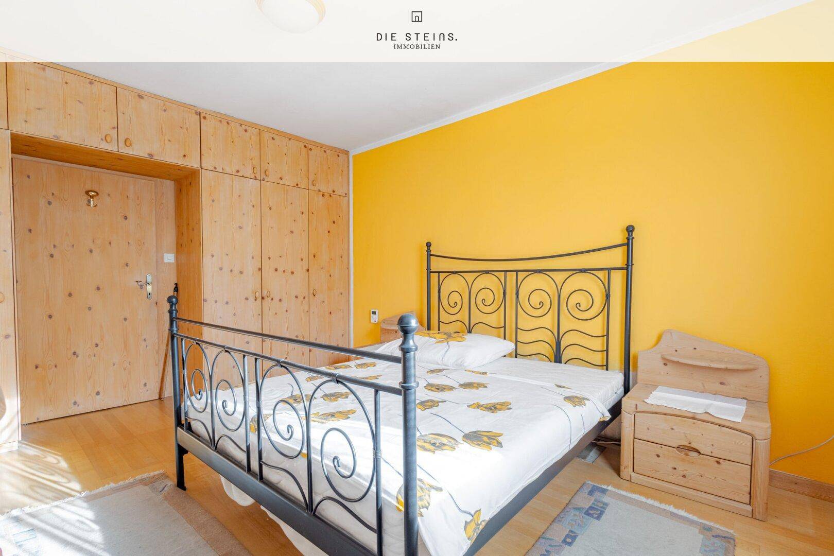 Schlafzimmer mit gelber Akzentwand, Einbauschränken aus Holz und schmiedeeisernem Bett.