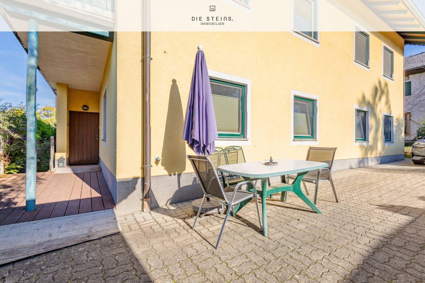 Gepflasterte Terrasse mit Gartenmöbeln und Sonnenschirm neben dem Haus.