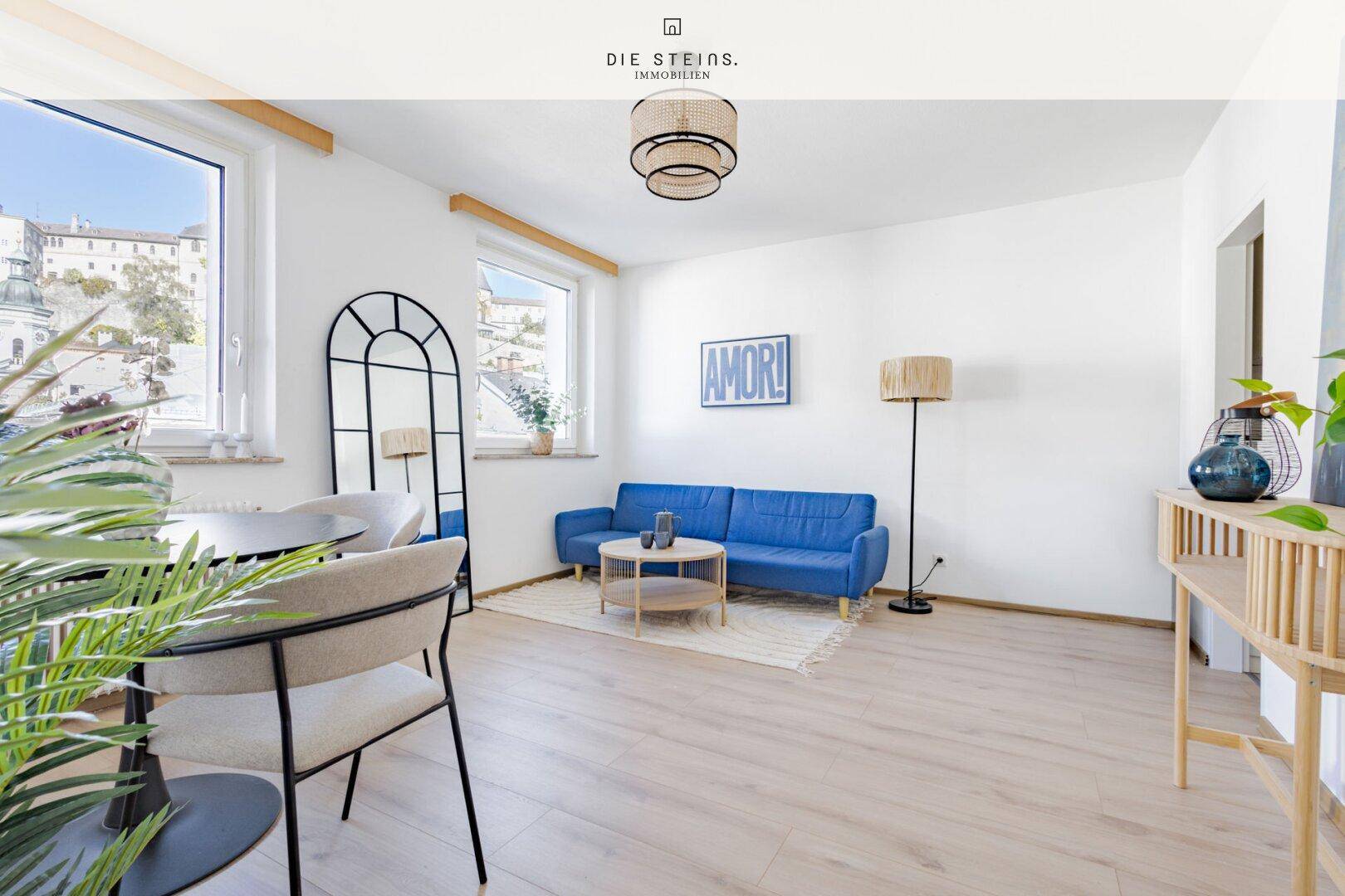 Geräumiges Wohnzimmer mit blauer Couch, Holzboden und viel Tageslicht.