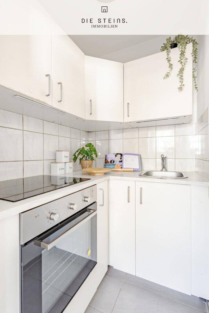 Kompakte, helle Küche mit weißen Schränken, Fliesenrückwand und modernen Geräten.