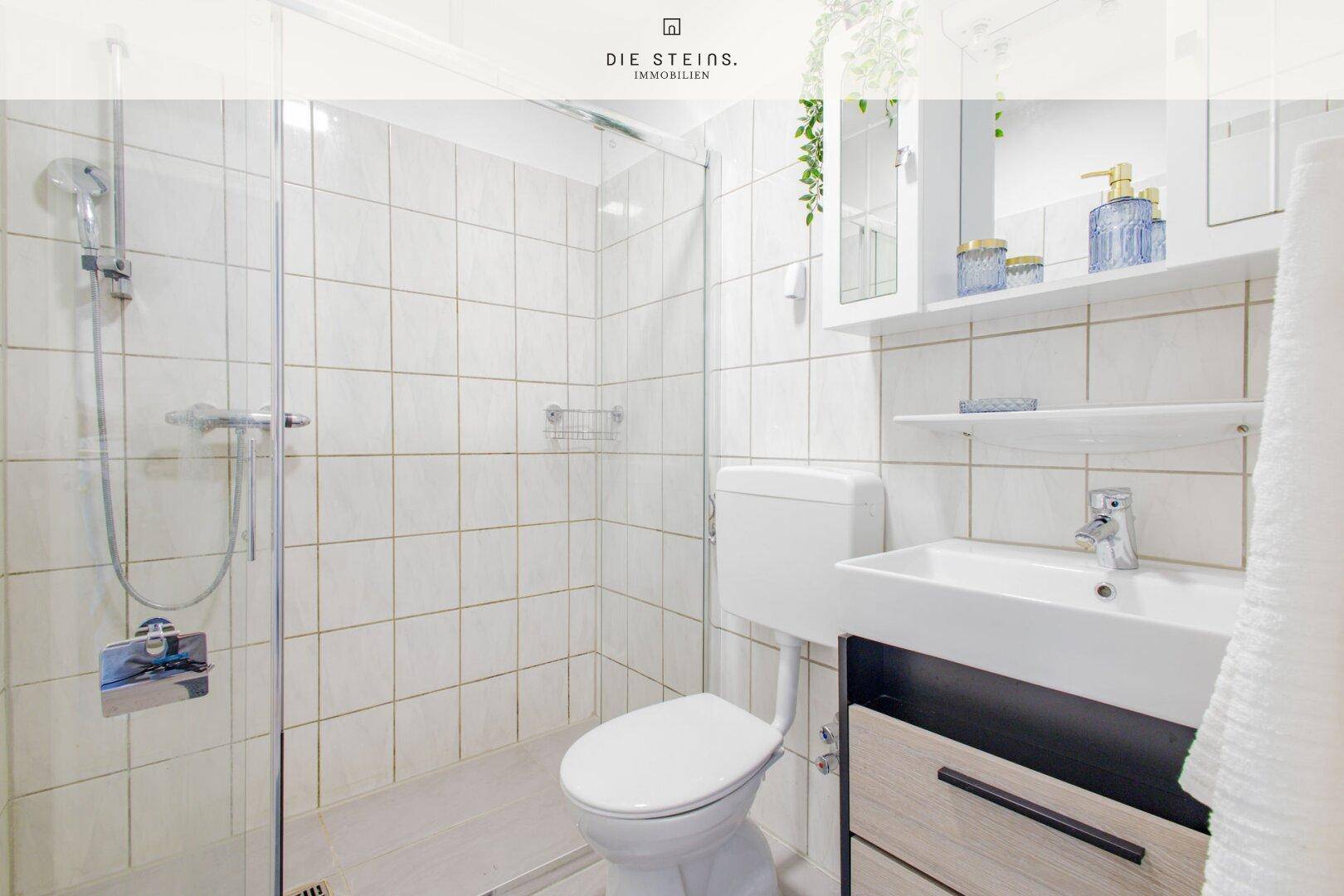 Modernes Badezimmer mit Dusche, WC, Waschbecken und hellen Fliesen.