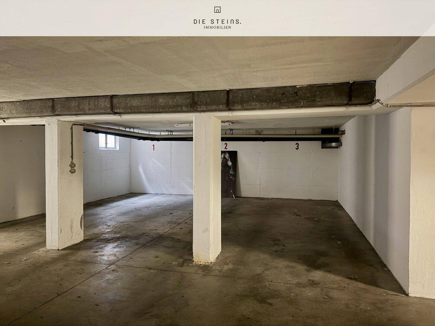 Große Tiefgarage mit Betonboden, tragenden Säulen und nummerierten Stellplätzen.