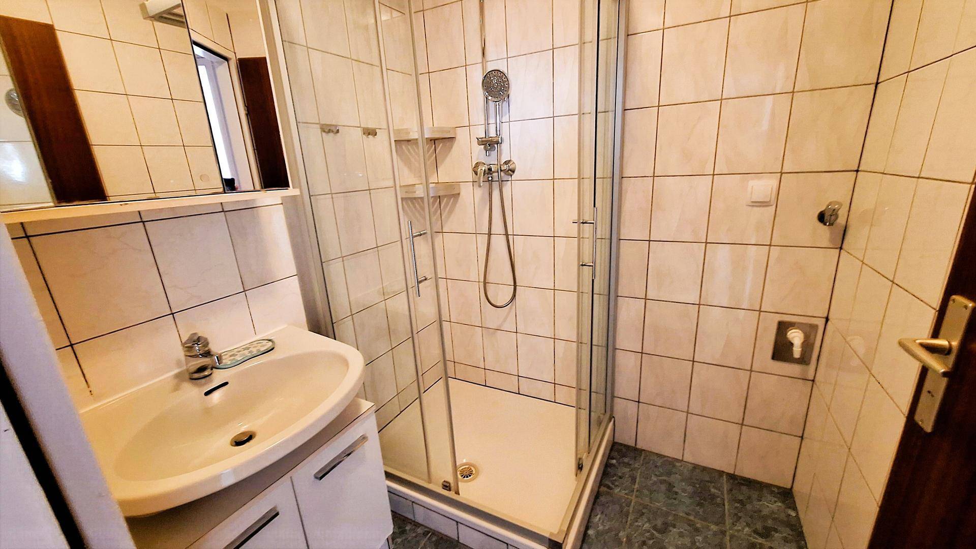 Badezimmer mit Duschkabine, Waschbecken und hellen Fliesen, funktional und gepflegt.