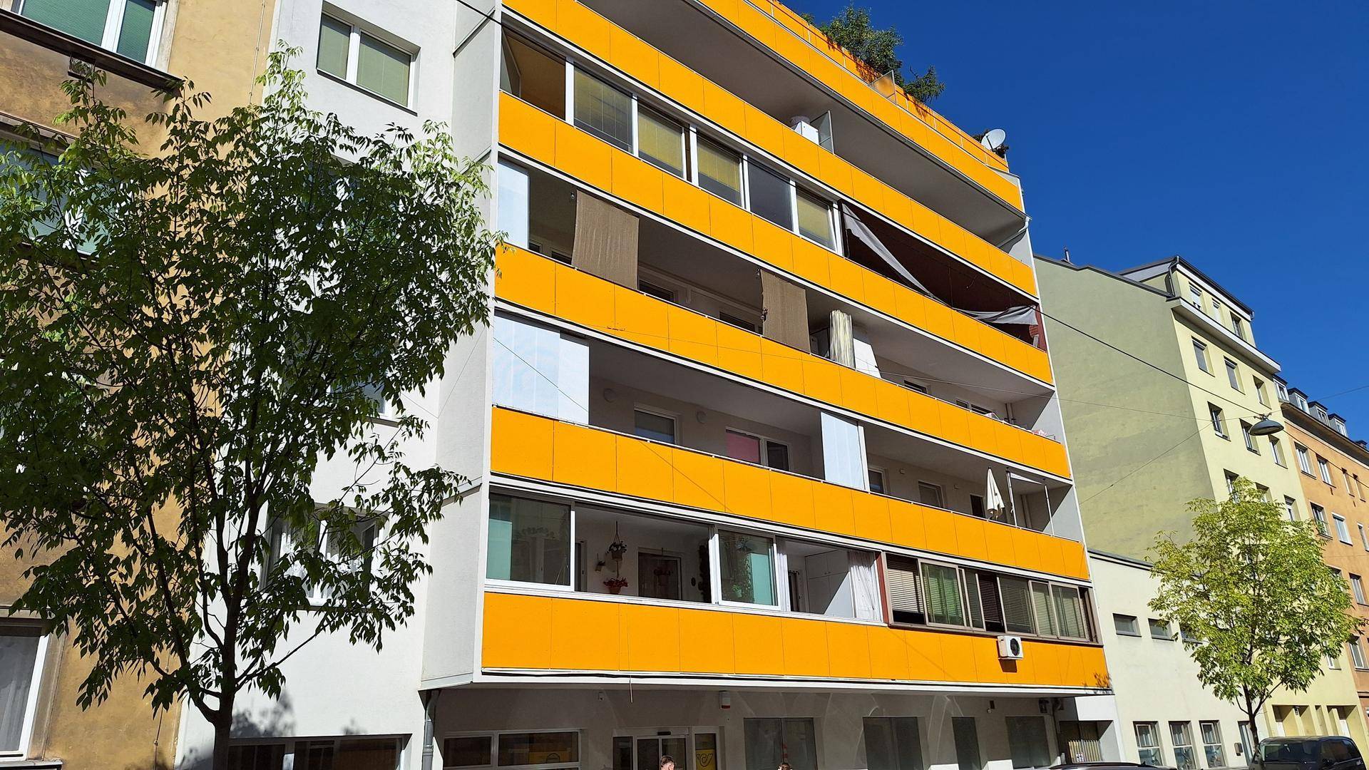 Mehrstöckiges Gebäude mit auffälligen gelben Balkonfronten und großen Fenstern unter blauem Himmel.