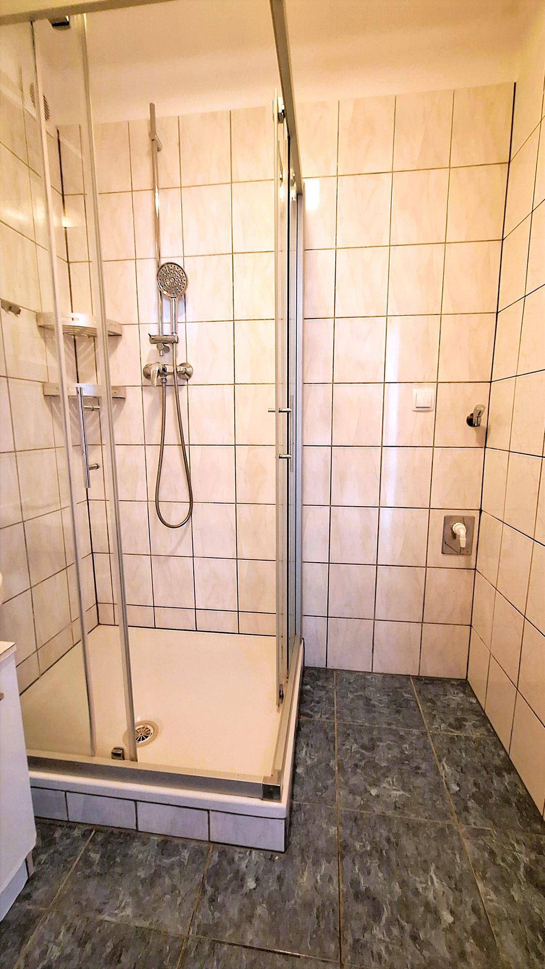 Duschbereich im Badezimmer mit Glasabtrennung und hellen Wandfliesen, sauber und funktional.