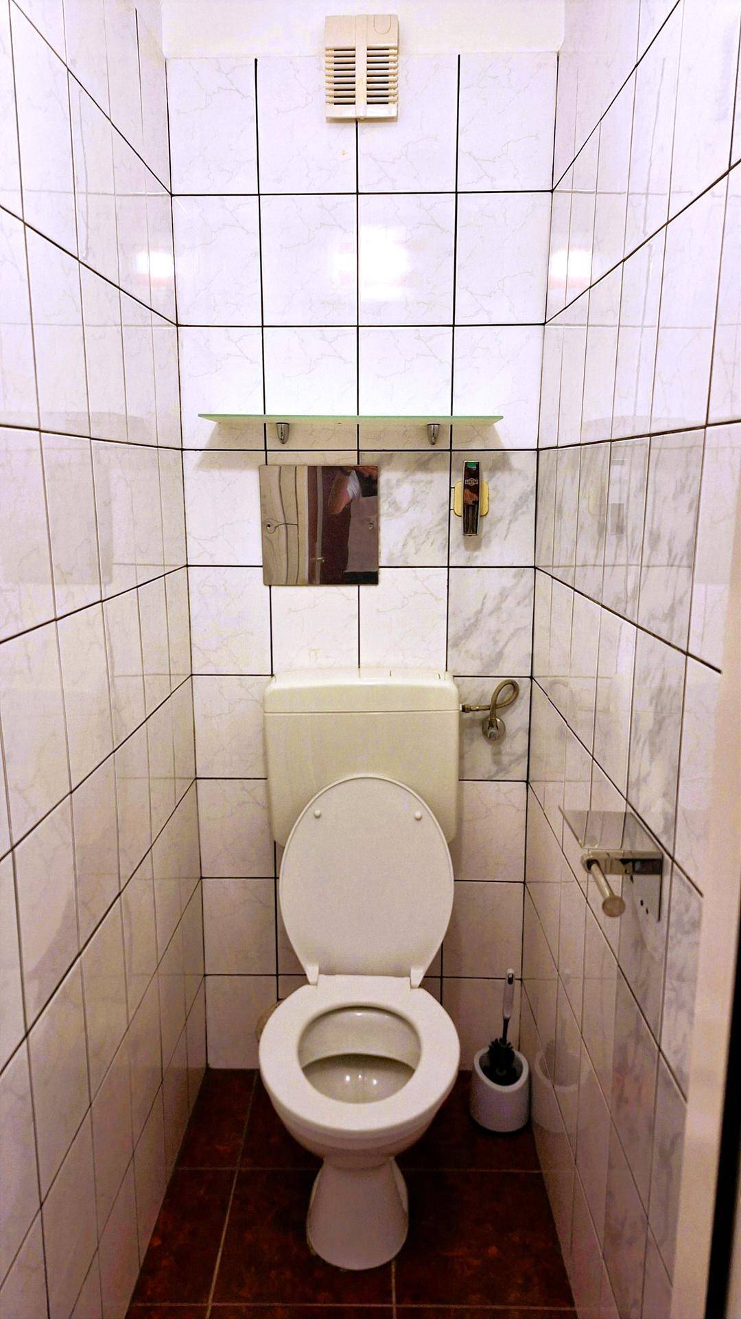 Separates WC mit weiß gefliesten Wänden und einer Toilette, ausgestattet mit Abluftventilator.