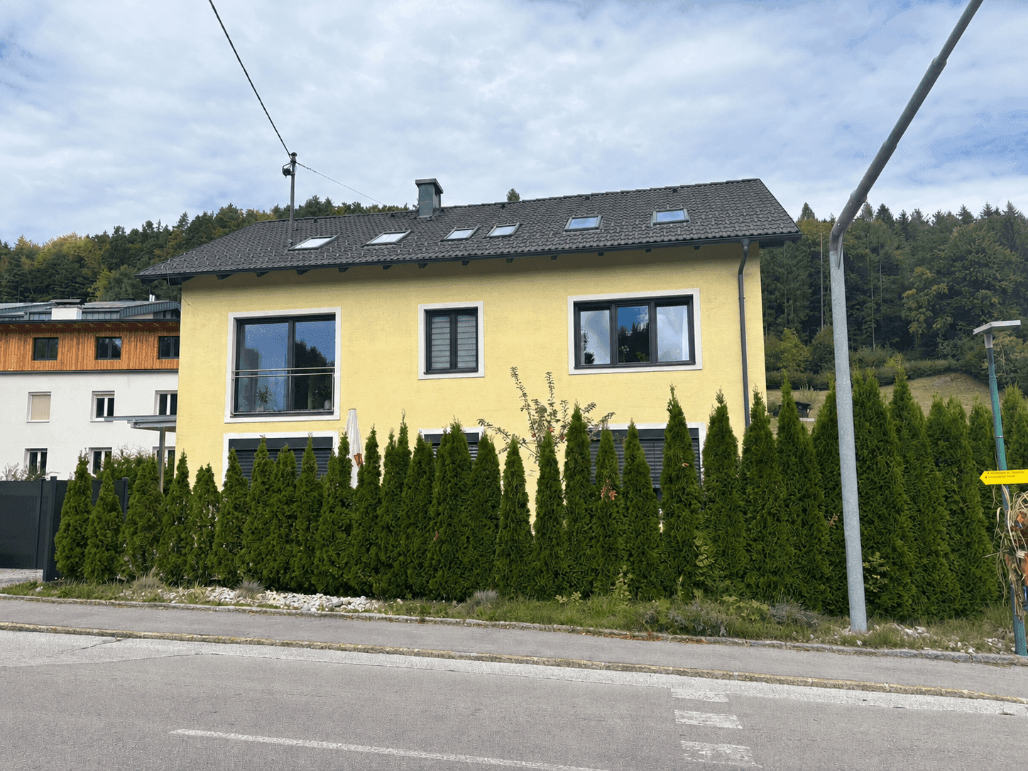 Gelbes Einfamilienhaus mit Satteldach, Dachfenstern und grüner Hecke zur Straße.