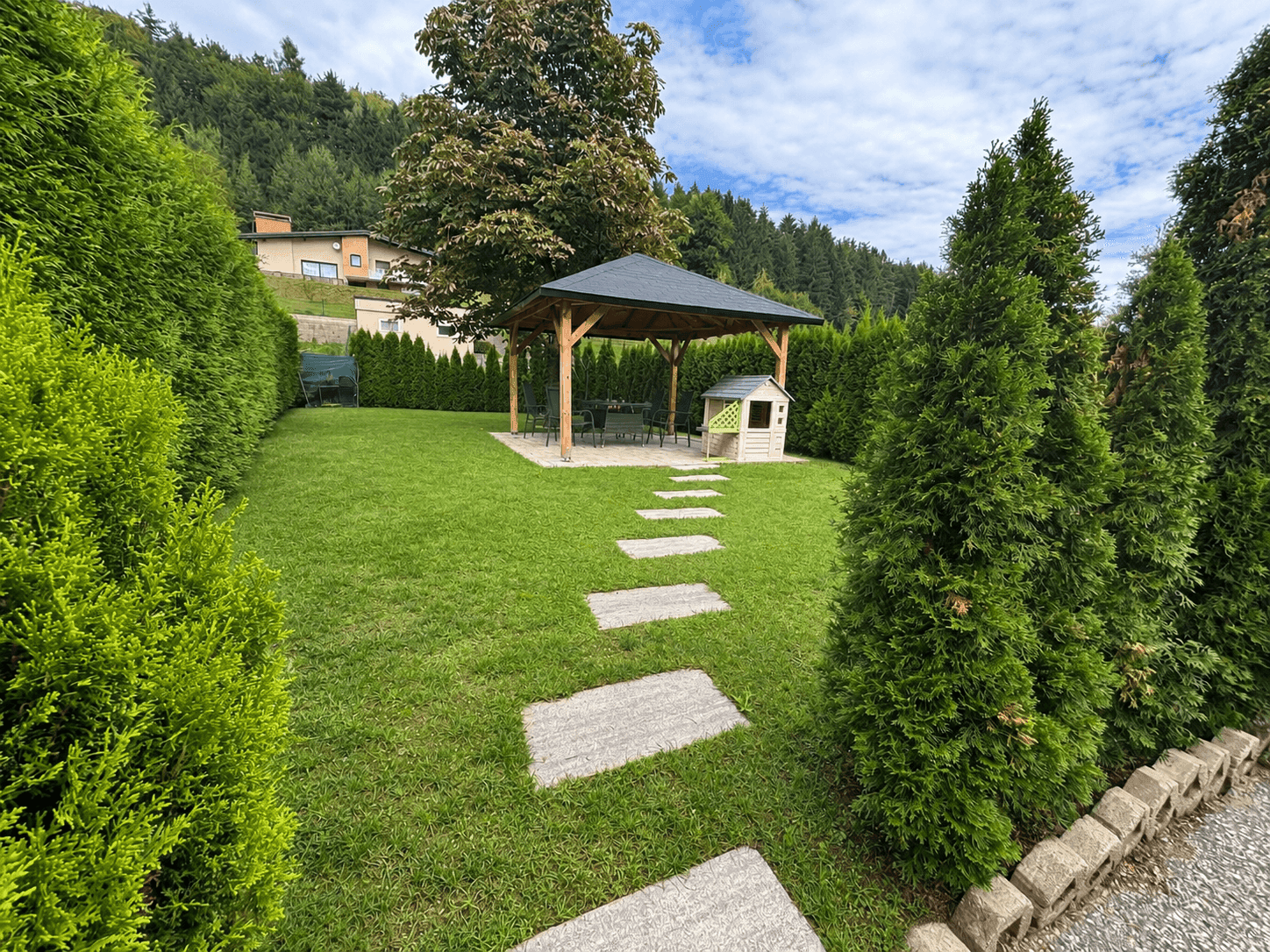 Gepflegter Garten mit Rasenfläche, Holzpavillon, Trittsteinen und Kinderspielhaus.