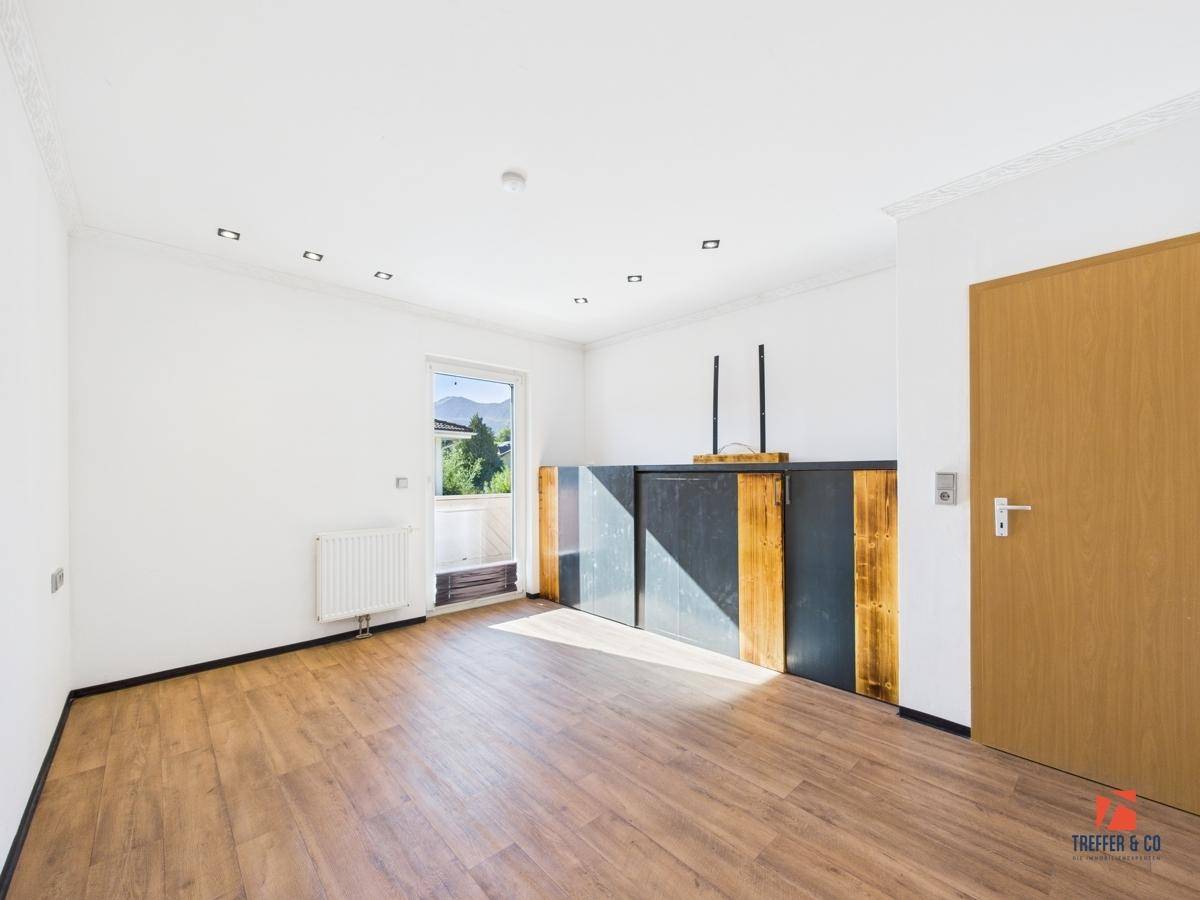 Helles Zimmer mit Laminatboden, Heizkörper und Zugang zu einem französischen Balkon.