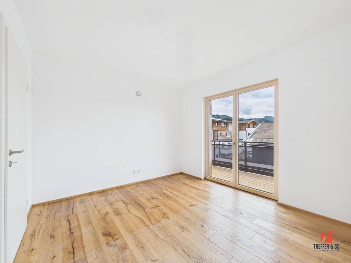 Helles Schlafzimmer mit Holzboden und Balkonzugang, bietet einen Blick auf die Nachbarschaft.