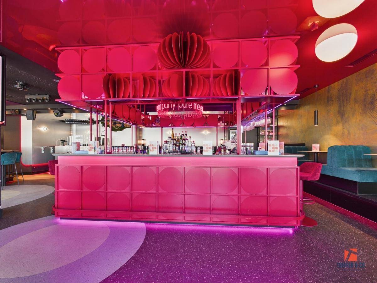 Auffällige pinke Bartheke mit integrierter Beleuchtung und modernem Design im Zentrum des Raumes.
