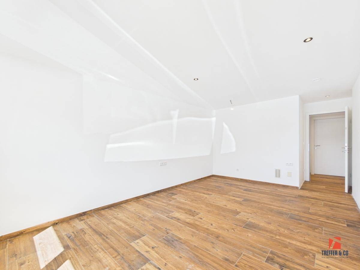 Geräumiges, helles Zimmer mit Holzoptik-Boden und indirekter Deckenbeleuchtung.