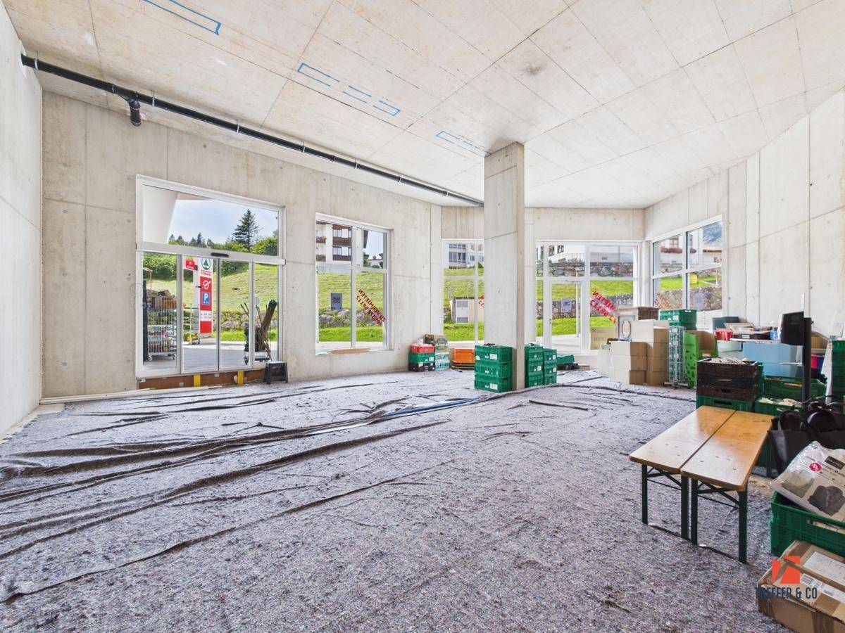 Geräumiger Gewerberaum im Rohbau mit großen Fenstern und Blick auf die grüne Umgebung.