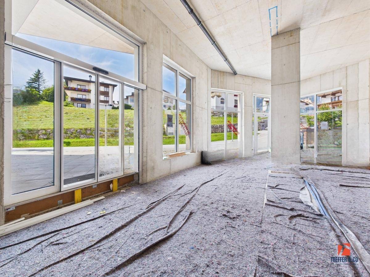 Eingangsbereich des unfertigen Raumes mit automatischer Glastür und Blick auf die umliegende Bebauung.