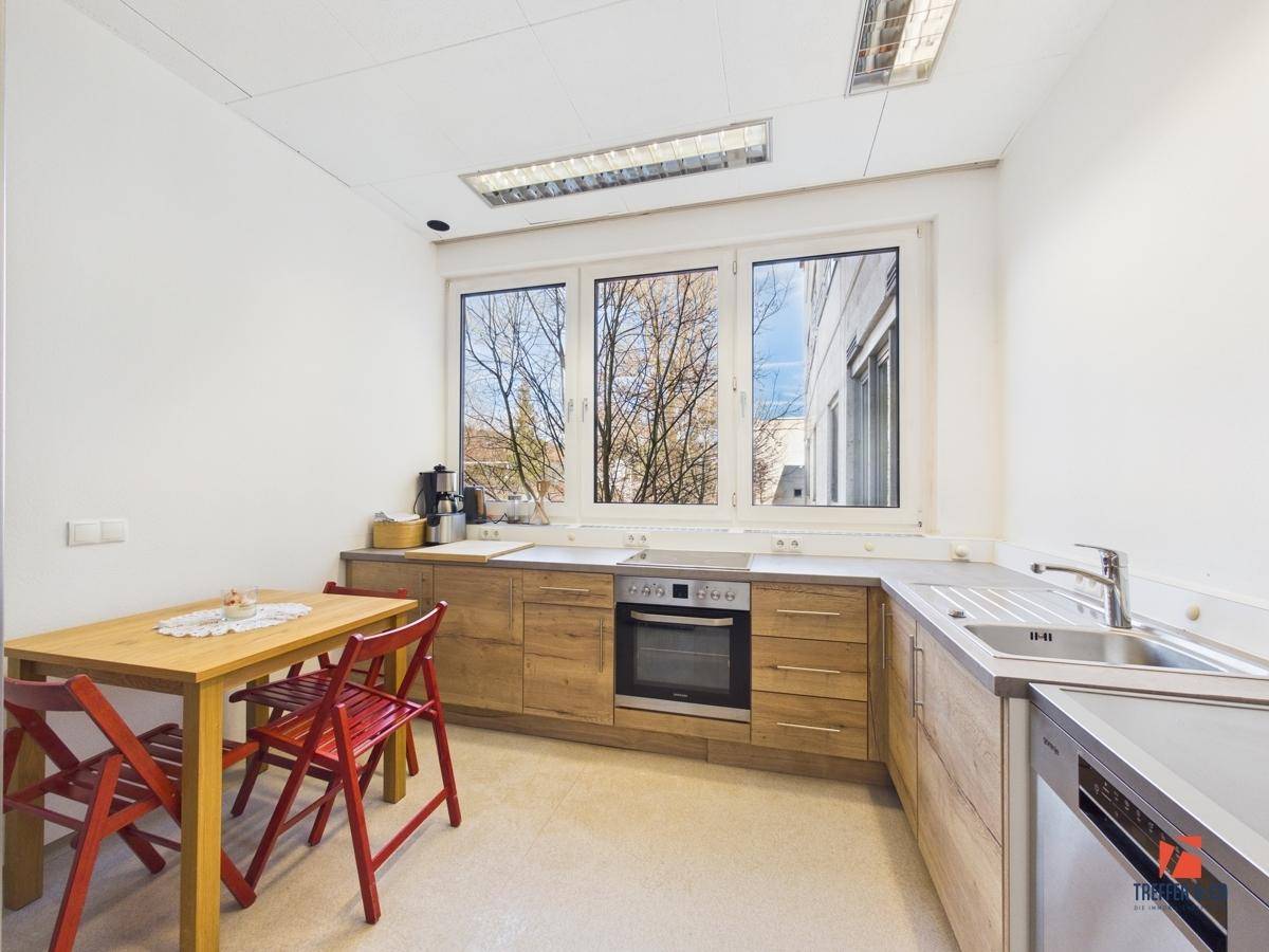 Funktionale Küche mit Holzschränken, Esstisch und Stühlen, sowie einem großen Fenster mit Ausblick.